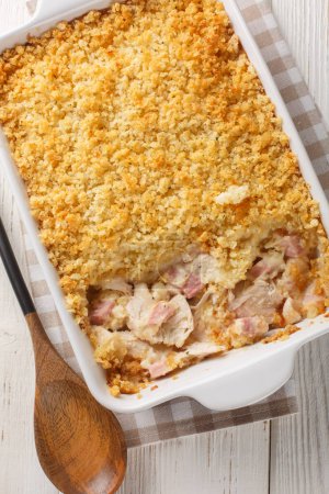 Chicken Cordon Bleu casserole with chicken, ham, and cheese baked in a light and creamy sauce topped with breadcrumbs close up in the baking dish on the wooden table. Vertical top view from abov