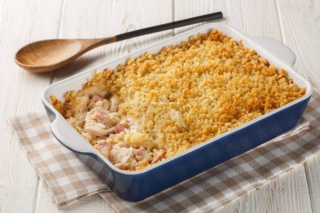 Chicken Cordon Bleu Casserole with chicken breast, chopped ham and Swiss cheese layered with creamy sauce and a buttery Panko breadcrumbs close up in the baking dish on the wooden table. Horizonta