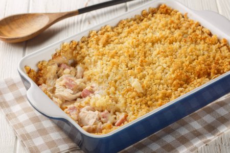 Chicken Cordon Bleu casserole layered together, it's a warm and comforting weeknight meal close up in the baking dish on the white wooden table. Horizonta