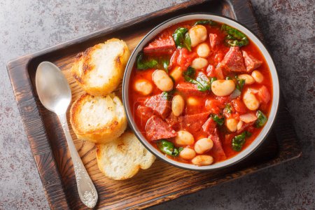 Crockpot stew with chorizo, butter bean and spinach close-up in a bowl served with toasted bread on the table. Horizontal top view from abov