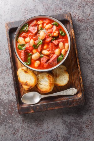 Chorizo, butter bean and spinach stew close-up in a bowl served with toasted bread on the table. Vertical top view from abov