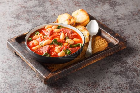 Würziger Eintopf aus Limabohnen, Chorizo und Spinat in Tomatensauce in Großaufnahme in einer Schüssel auf dem Tisch. Horizonta