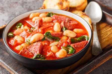 Spanish stew of butter beans, chorizo and spinach in tomato sauce close-up in a bowl on the table. Horizonta