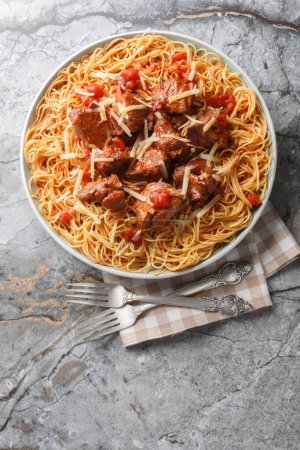 Langsam geschmortes Rindfleisch in Weintomatensauce, serviert mit Spaghetti in Großaufnahme auf einem Teller auf dem Tisch. Vertikale Ansicht von oben