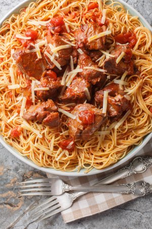 Estofado de ternera kokkinisto mediterráneo en salsa de tomate de vino picante servido con espaguetis de cerca en un plato sobre la mesa. Vista superior vertical desde arriba