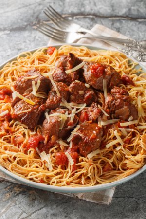 Langsam geschmortes Rindfleisch in Weintomatensauce, serviert mit Spaghetti in Großaufnahme auf einem Teller auf dem Tisch. Vertica