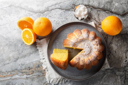 Delicious orange pound cake with zest and orange juice, sprinkled with powdered sugar on a plate on the table. Horizontal top view from abov