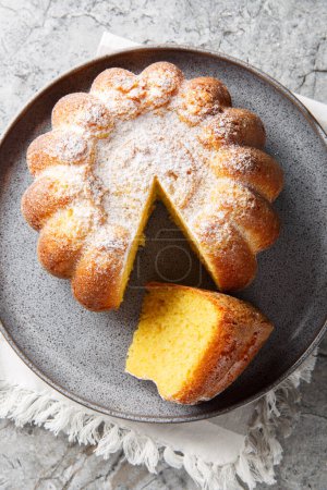 Close-up of Meskouta orange pound cake with powdered sugar on a plate on the table. Vertical top view from abov