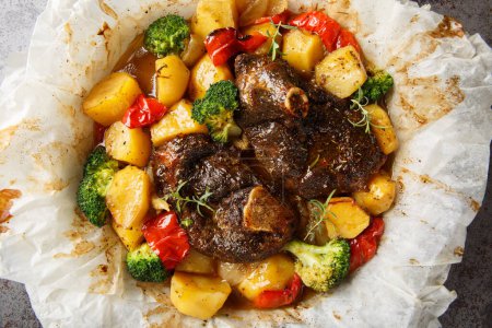 En papillote Lamb with potatoes, broccoli, onions and peppers in parchment close-up in a frying pan on the table. Horizontal top view from abov
