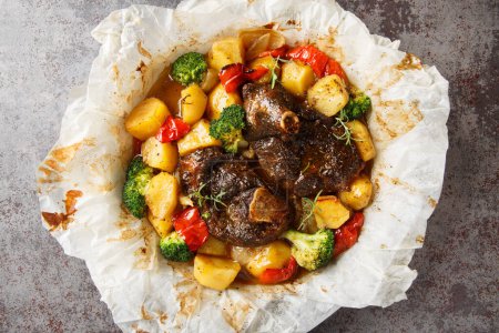 Baked Lamb with potatoes, broccoli, onions and peppers in parchment close-up in a frying pan on the table. Horizontal top view from abov
