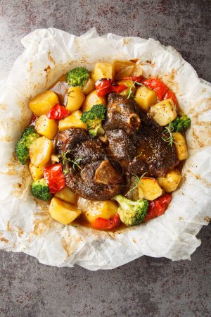 Lamb baked with vegetables and herbs in parchment close-up in a frying pan on the table. Vertical top view from abov