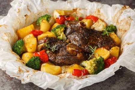 Cordero al horno con patatas, brócoli, cebollas y pimientos en pergamino de cerca en una sartén sobre la mesa. Horizonta