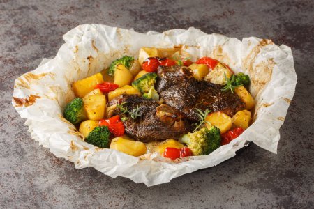 Lammfleisch in eigenen Säften mit Kartoffeln, Brokkoli, Zwiebeln und Paprika in Pergament in Großaufnahme in einer Pfanne auf dem Tisch gekocht. Horizonta