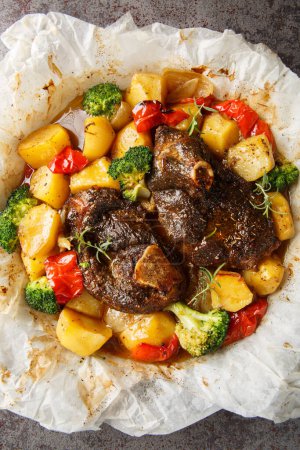 Slow Cooked lamb with potatoes, broccoli, onions and peppers in parchment close-up in a frying pan on the table. Vertical top view from abov