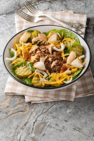 Cheeseburger salad with romaine lettuce, ground beef, pickles, cheddar cheese and croutons close-up in a bowl on the table. Vertica