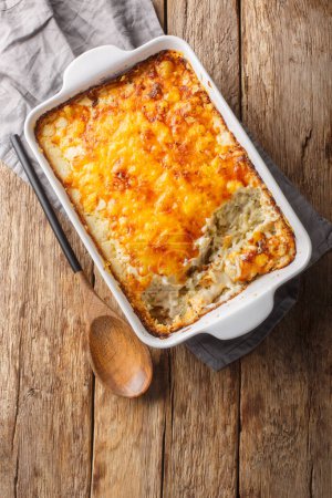 Hashbrown casserole with thickened creamy chicken soup and cheddar cheese close-up in a baking dish on the table. Vertical top view from abov