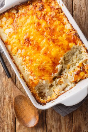 Hash brown potato casserole with creamy chicken soup and cheddar cheese close-up in a baking dish on the table. Vertical top view from abov