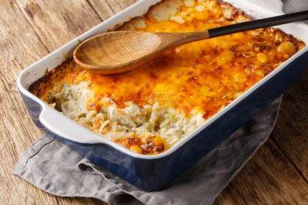 Hash brown casserole is quick and easy comfort food made with oven-baked cheesy potatoes in cream of chicken closeup in the baking dish on the wooden table. Horizonta