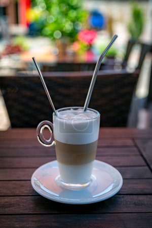 Téléchargez les photos : Un latte macchiato dans un verre sur une soucoupe blanche avec une paille métallique et une cuillère métallique avec un fond coloré - en image libre de droit