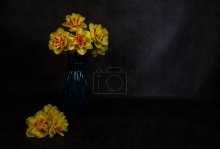 Photo for A still life with a blue vase with yellow daffodils with an orange heart on a dark background - Royalty Free Image