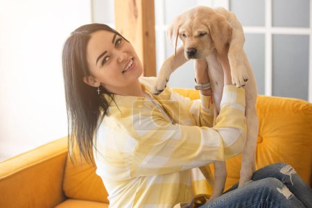 Photo for A small Labrador puppy in the arms of his owner in a yellow plaid shirt - Royalty Free Image