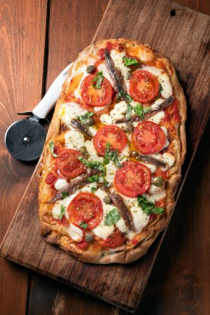 Foto de Deliciosa pizza romana con anchoas, alcaparras, mozzarella y tomate, comida italiana - Imagen libre de derechos