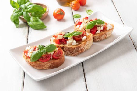 Tablett mit köstlichen Caprese Bruschette, eine typisch italienische Vorspeise mit Mozzarella, Tomaten, Basilikum, schwarzen Oliven, Oregano und Olivenöl