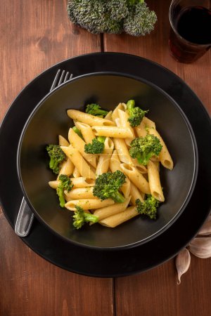 Photo for Top view of a plate of delicious pasta with broccoli, isolated on wooden background, vegetarian Italian food - Royalty Free Image
