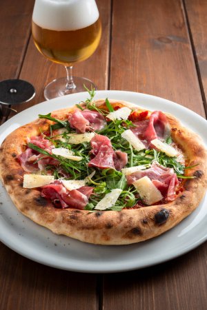 Foto de Deliciosa pizza gourmet con jamón, copos de grana y ensalada de cohetes, comida italiana - Imagen libre de derechos