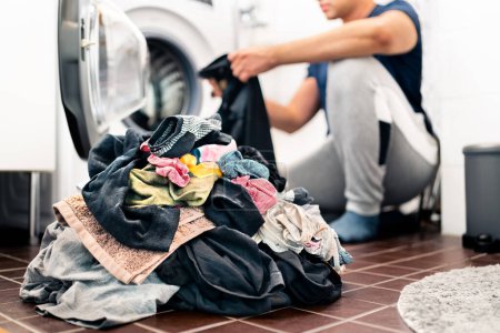 Photo for Laundry, washing clothes. Man loading washer machine and sorting by color and fabric.  Male homemaker doing house chores. Domestic work in family. Young dad and parent putting clothing in dryer. - Royalty Free Image