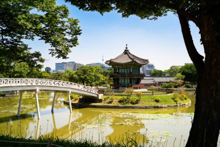 Photo for South Korea, Seoul. Gyeongbokgung palace area garden and park. Hyangwonjeong pavilion and bridge. City skyline in the background. Summer travel and tourist attraction. Beautiful Korean landscape. - Royalty Free Image