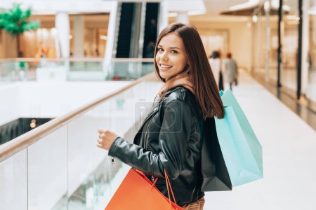 Foto de Woman shopping. Young woman with shopping bags walking in the mall. Spring style clothing. Consumerism, consumer lifestyle, spring sales concept. - Imagen libre de derechos