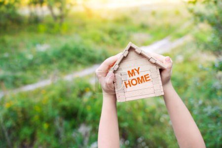 My home background. House construction, home for the family. Concept with kid's hands holding little wooden house with text My home. 