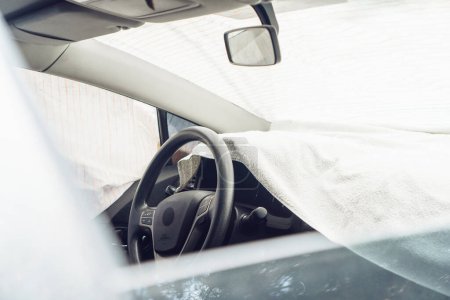 Téléchargez les photos : Protection contre le chauffage de la voiture. Sauver la voiture de la chaleur estivale en couvrant le tableau de bord et le pare-brise avec des chiffons. - en image libre de droit