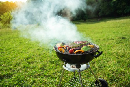 Photo for Grilled meat in grill. Roasting steaks and vegetables bbq in a round grill in a meadow. Summer picnic outdoors. - Royalty Free Image