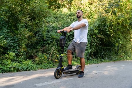 Photo for Handsome man with beard riding an electric scooter in the park - Royalty Free Image