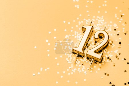 Téléchargez les photos : 12 ans de célébration fond festif fait avec une bougie dorée en forme de nombre Douze couché sur des étincelles. Bannière universelle de vacances avec espace de copie. - en image libre de droit