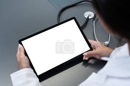 Doctor looking at blank mockup tablet computer with white screen for copy space. Background for medical product presentation or online medicine scene.