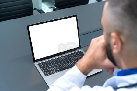 Doctor looking at blank mockup laptop with white screen for copy space. Background for medical product presentation or online medicine scene.