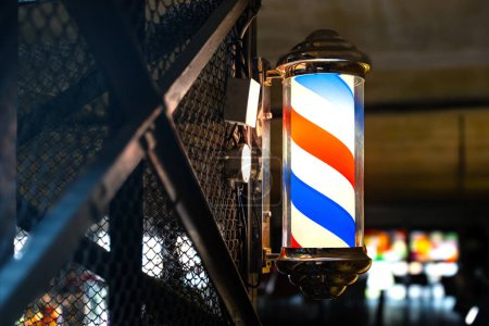 Barber pole of barbershop on vintage industrial wall in the evening. Classic barbershop spinning cylinder to attract customers.