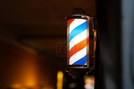 Barber pole of barbershop in the evening. Classic barbershop spinning cylinder to attract customers. Background with copy space.
