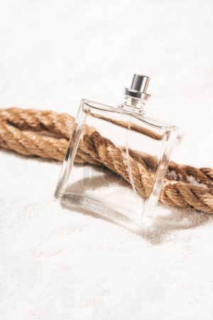 Nautical fragrance concept with perfume bottle lying on sand and rope. Vertical photography.