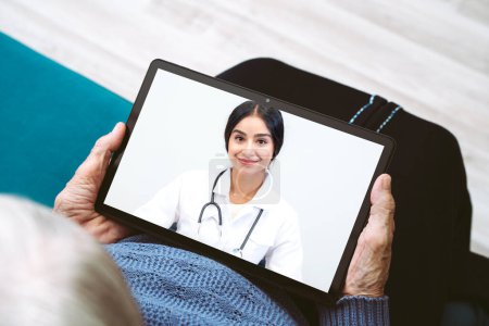 Online medicine with remote medical assistance for elderly woman patient holding tablet computer having consultation online with young female doctor.