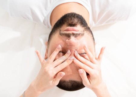 Massage du visage masculin pour réduire les poches par un massothérapeute professionnel en clinique de beauté