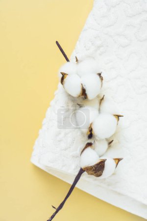Nahaufnahme einer zarten Baumwollblume auf einem weißen Handtuch vor gelbem Hintergrund. Konzept von Frische und Sauberkeit zu Hause.