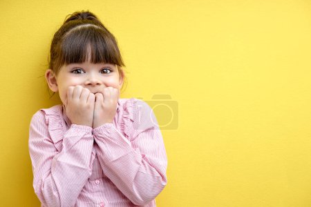 Photo for Little child girl is surprised by something, holding hands on cheek. cute kid in pink blouse in shock, isolated on yellow studio background - Royalty Free Image