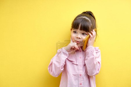 Téléchargez les photos : Funny child girl talking on phone with someone, thinking. Caucasian kid looking at side, concentrated in thought. portrait of child having serious talk - en image libre de droit