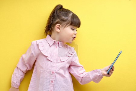 Foto de Side view on angry child girl emotionally talking on smartphone via online conversation, arguing, speaking. isolated yellow background - Imagen libre de derechos