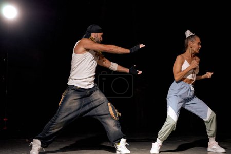 Foto de Stylish man and woman dancing hip-hop in casual clothes on black studio background at dance hall with white light. Youth culture, hip-hop, movement, style and fashion, action. Fashionable portrait. - Imagen libre de derechos