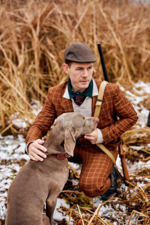 Photo for Hunting period, autumn season open. man hunter with gun in fashionable suit, in search of a trophy. caucasian man sit with weapon and hunting dog tracking down the game, sitting together. - Royalty Free Image